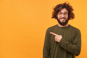 Closeup of a bearded young guy looks delighted gladden amazed pointing with index finger aside on...