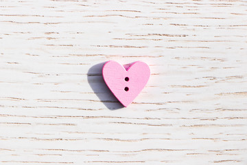 Pink heart in the center of the image on a white wooden surface. Background to the Valentine's day and wedding.