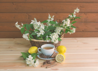 Basket with white jasmine flowers, cup of green tea, lemons and spices on wooden table