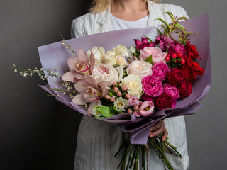 A beautiful bouquet of rare flowers with lisianthuses, ranunculus, carnations, peony roses, in the hands of a girl in white clothes with blond hair.