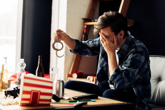 Embarrassed Man Covering Face While Holding Handcuffs After Party