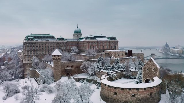 Budapest, Hungary - 4K flying up on a snowy winter morning at Buda Castle Royal Palace with Szechenyi Chain Bridge and Parliament at background