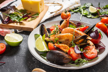 Fresh seafood salad, mussels, shrimp, fresh vegetables and herbs on stone background