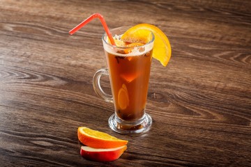 Red hot alcohol vine beverage with fruits or juice and spices (sangria, grog, punch, toddy, glintwine) in a glass decorated by orange slice on a on dark wooden table decorated by apple, warm