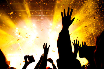 Hands raised up in the crowd of music show in the warm lights of stage. Confetti in the air
