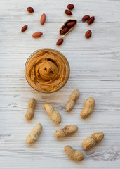 Bowl of peanut butter on a white wooden table, top view. From above, overhead, flat lay.