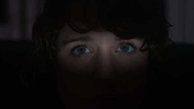 A Young woman's worried eyes are spotlighted, moody shadowy environment