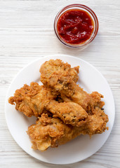 Fried chicken legs on a white round plate with ketchup, top view. From above, flat lay.