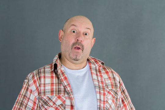 a man without hair and a plaid shirt is very surprised