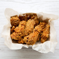 Fried chicken wings in paper box over white wooden background. Top view, overhead. Close-up.