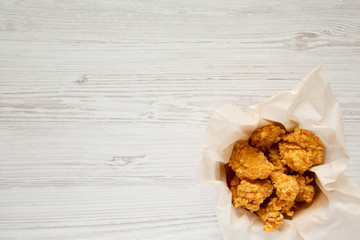 Fried chicken bites in paper box over white wooden surface, top view. Flat lay, overhead, from above.