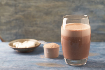 Glass of Chocolate Protein Shake with milk and banana. Whey protein in scoop and BCAA amino acids in background. Sport nutrition.Wooden background. Copy space. 