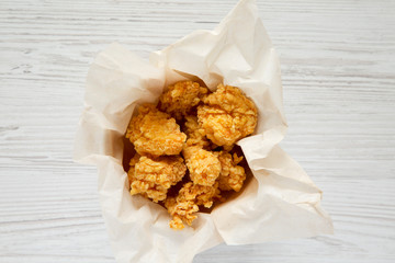 Fried chicken bites in paper box over white wooden background. Flat lay, overhead, top view.