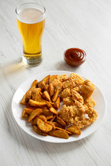 Fast food: fried potato wedges, chicken bites on a white plate, beer and barbecue sauce on a white wooden surface, low angle view. Close-up.