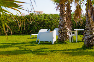 Wonderful garden with palm trees and comfortable armchairs used by tourists to take a relaxing aperitif.