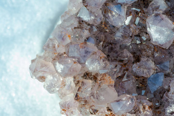 Amethyst natural crystal cluster with Goethite inclusions from Brazil on white snow at a sunny winter day.