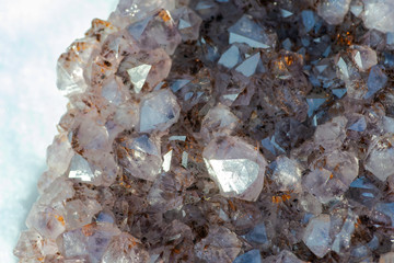 Amethyst natural crystal cluster with Goethite inclusions from Brazil on white snow at a sunny winter day.