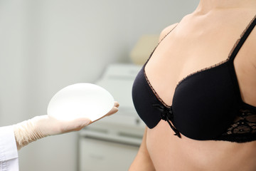 Doctor showing silicone implant for breast augmentation to patient in clinic, closeup. Cosmetic...