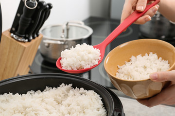 Woman putting boiled rice into bowl from cooker in kitchen, closeup