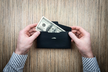 investing money dollars in an envelope with male hands on a wooden background.