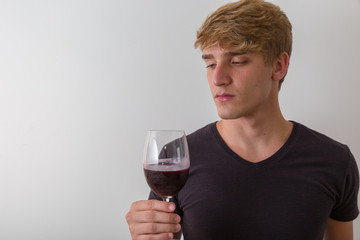 Concentrated young man sommelier with red wine in glass over white background