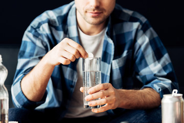 cropped view of man suffering from hangover holding aspirin and glass of water in hands