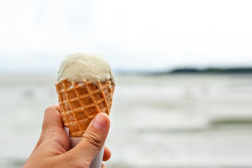 A hand holding a cone with vanilla ice cream