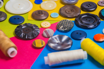 A small pile of retro buttons with threads lies on a colorful, cheerful background.