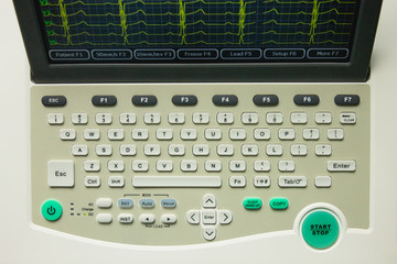 Electrocardiograph medical device with screen and keyboard, top view. Screen showing yellow cardiography heart rythm leads.