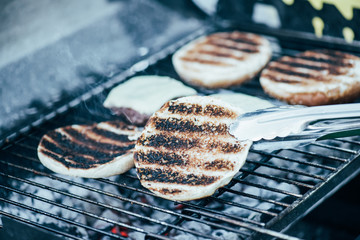 selective focus of tweezers and delicious fresh burgers ingredients with crust grilling on barbecue grid