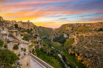 Fototapeta na wymiar Two women enjoy a sunset meal on a terrace in the ancient city of Matera, Italy, overlooking the sassi caves, canyon ravine and the Convent of Saint Agostino