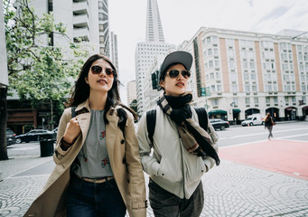 two asian college girls going to university together walking in front ground of university school in busy area san francisco. group of sisters in sunglasses standing with transamerica pyramid in back