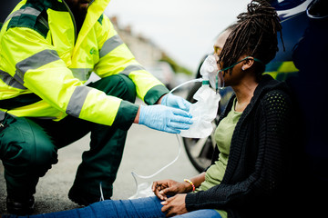 Male paramedic putting on an oxygen mask to an injured woman on a road