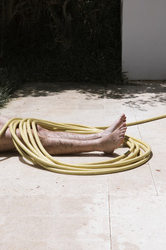Homme allongé au sol sous un tuyau enroulé