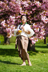 Femme debout en habit traditionnel devant des sakuras en fleurs