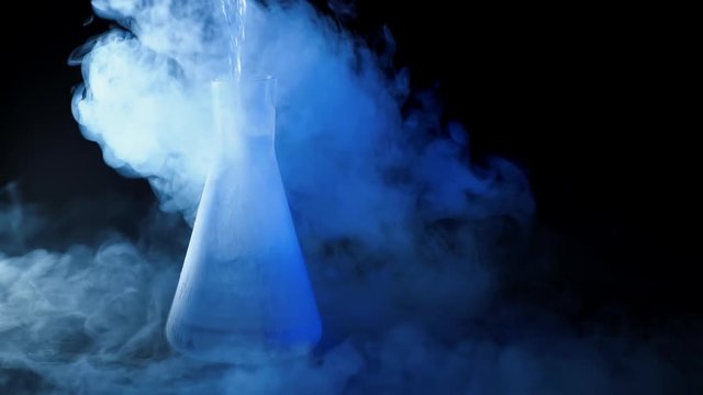 Flask with liquid nitrogen on black background. Concept of chemical experiments and tests. Edutainment. Copy space