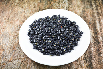 Black bean grain seeds on white plate food on wooden background