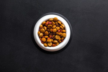 Dry dog food in bowl on black backgorund top view copy space