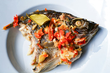 Cooking food tilapia fish head steamed with herb chilli sauce spicy topped on white plate