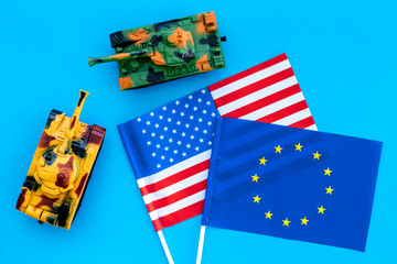 War, confrontation concept. European Union, USA. Tanks toy near european and american flag on blue background top view