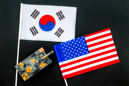 War, confrontation concept. Korea, USA. Tanks toy near korean and american flag on black background top view