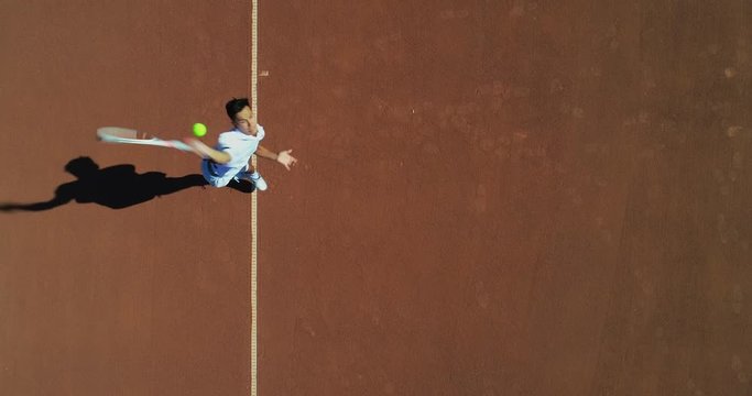 An Asian Tennis player serves and runs forward for return on a clay tennis court.