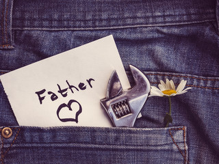 Wildflowers, paper note with the word FATHER and a painted heart on the background of a jeans pocket. Close-up, top view. Beautiful card for your beloved father