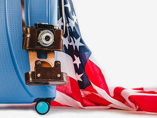 Stylish, blue suitcase, USA flag, vintage camera in a leather case on a white background, isolated. Close-up. Preparing for the summer trip