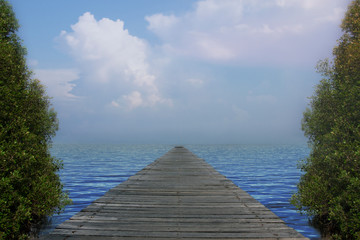Wooden bridge extends to the sea with mountain against blue sky. 