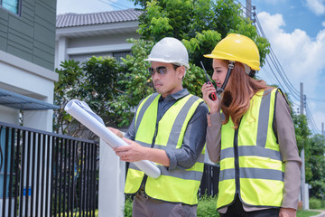 Asian engineers holding blueprint in their hands discussing plan with house inspectors to prepare for delivery to customers.