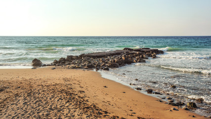 Empty beach with footsteps, some rocks in sea, in evening few moments before sunset. Lapta, Northern Cyprus