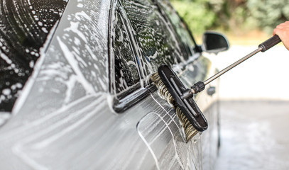 Side of silver car washed in self serve carwash. Detail on brush leaving strokes in shampoo foam.