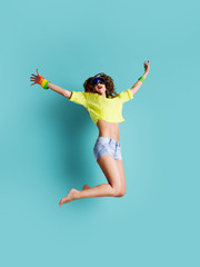 Colorful dressed hipster girl jumps on minimal pop art blue background