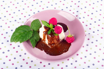 Cream pudding with chocolate sauce, raspberry and mint on beautiful multicolored tablecloth.